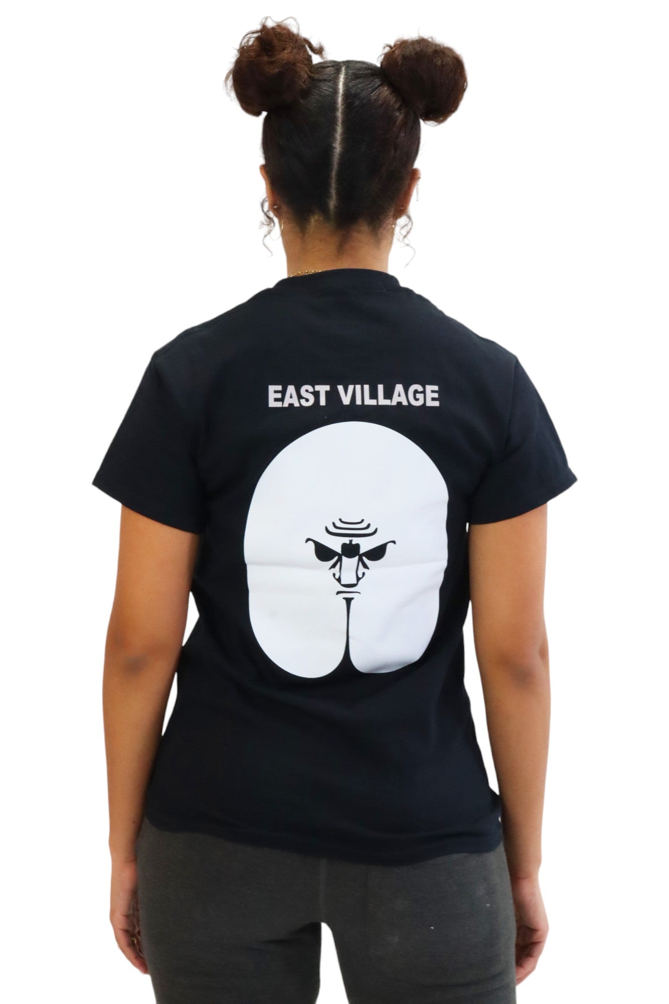 Back view of a woman in a black t-shirt. The back has a large white graphic of a butt with an angry face drawn in the center, and the words 'EAST VILLAGE' above it.