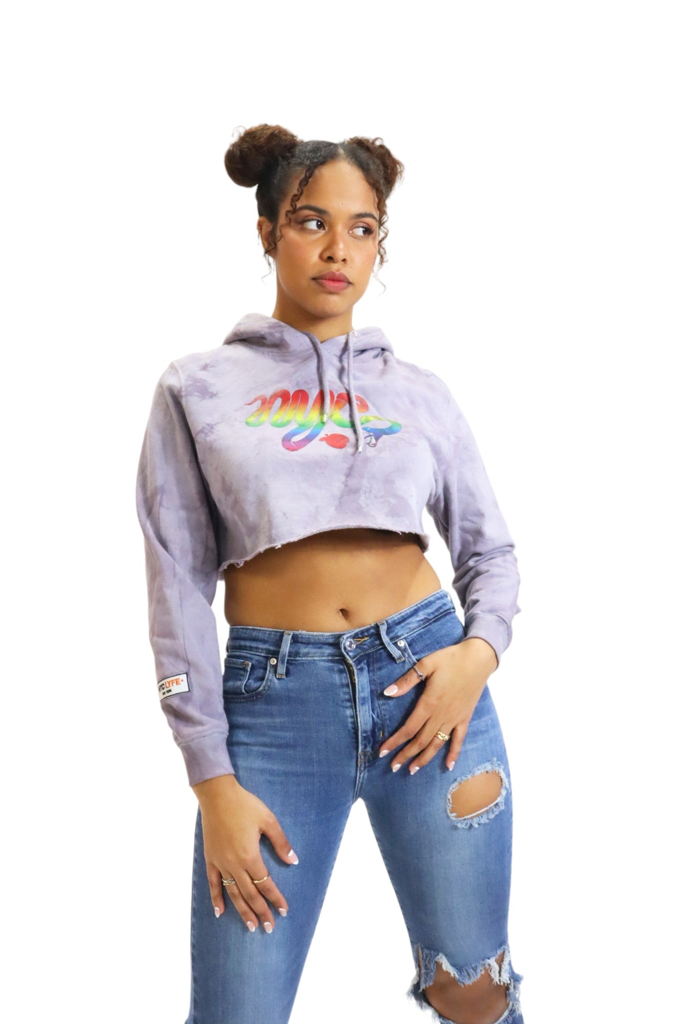 A woman models a lavender tie-dye cropped hoodie and ripped jeans. The hoodie has a rainbow-colored 'nyc' snake graphic on the chest.