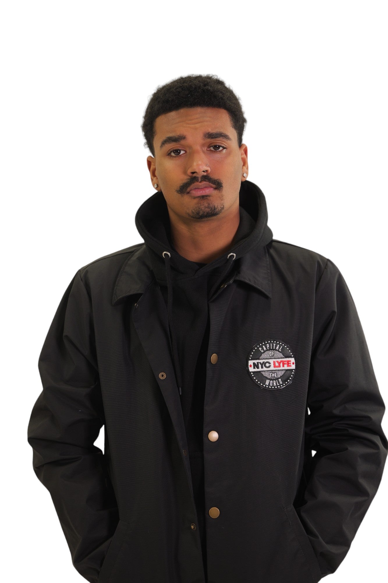 Front Close Up view of a model wearing a black coach's jacket. On the left chest is a circular embroidered patch with the words 'Original NYC LYFE'.