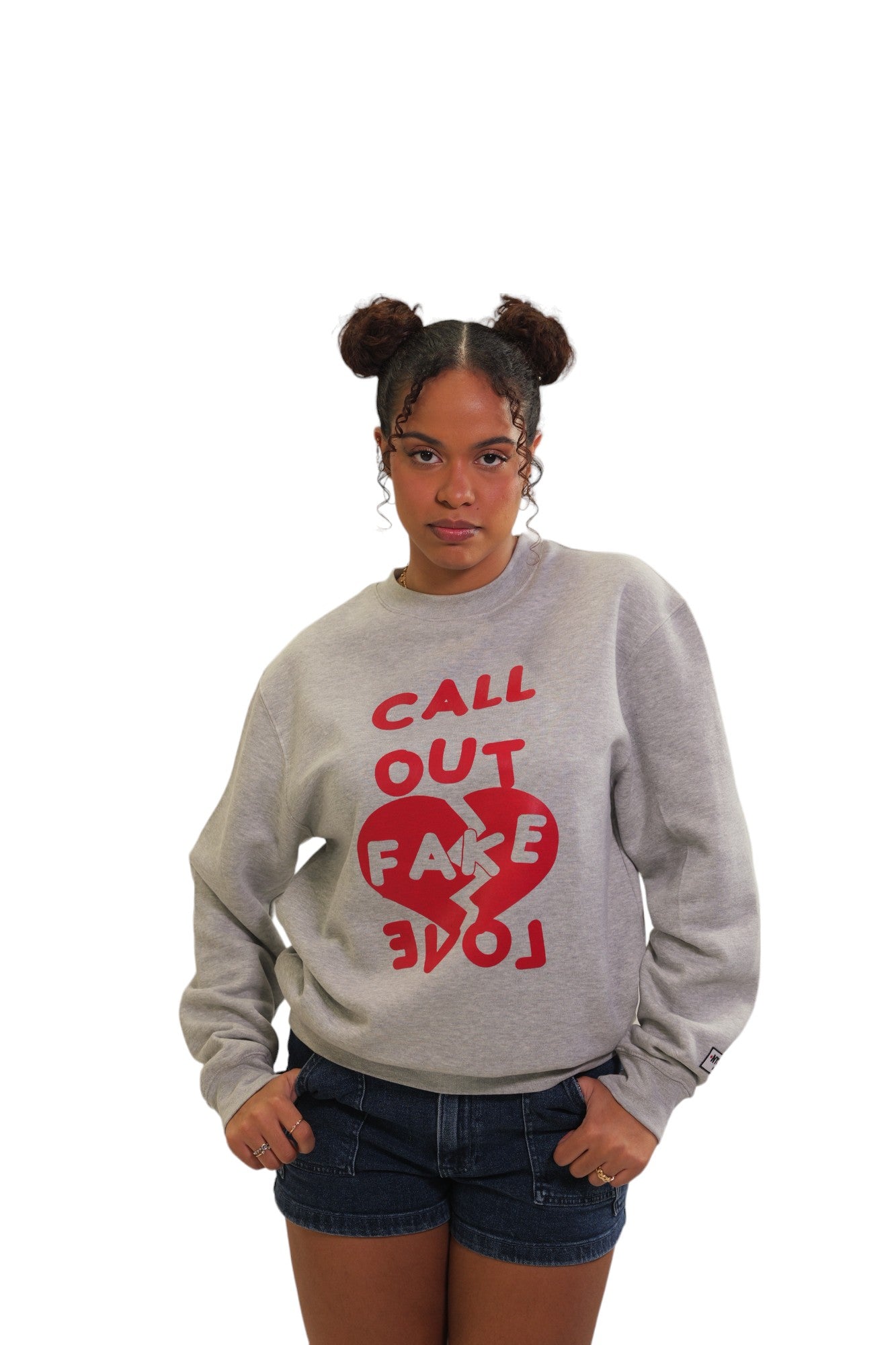 A woman models a heather grey crewneck sweatshirt. It features the words 'CALL OUT FAKE LOVE' in bold, red text with a graphic of a broken red heart between the words.