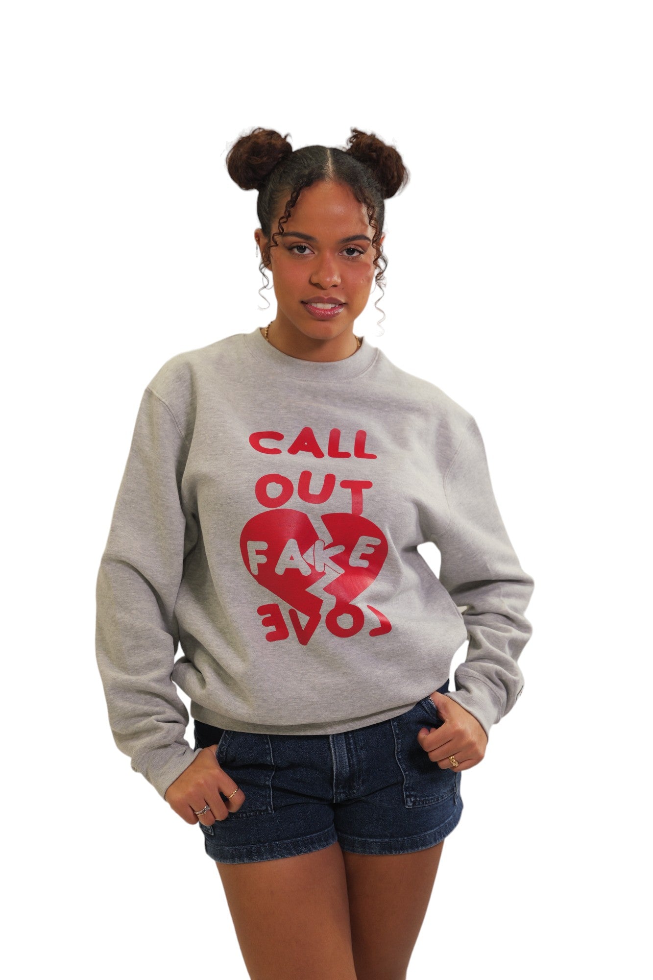 A woman models a heather grey crewneck sweatshirt. It features the words 'CALL OUT FAKE LOVE' in bold, red text with a graphic of a broken red heart between the words.