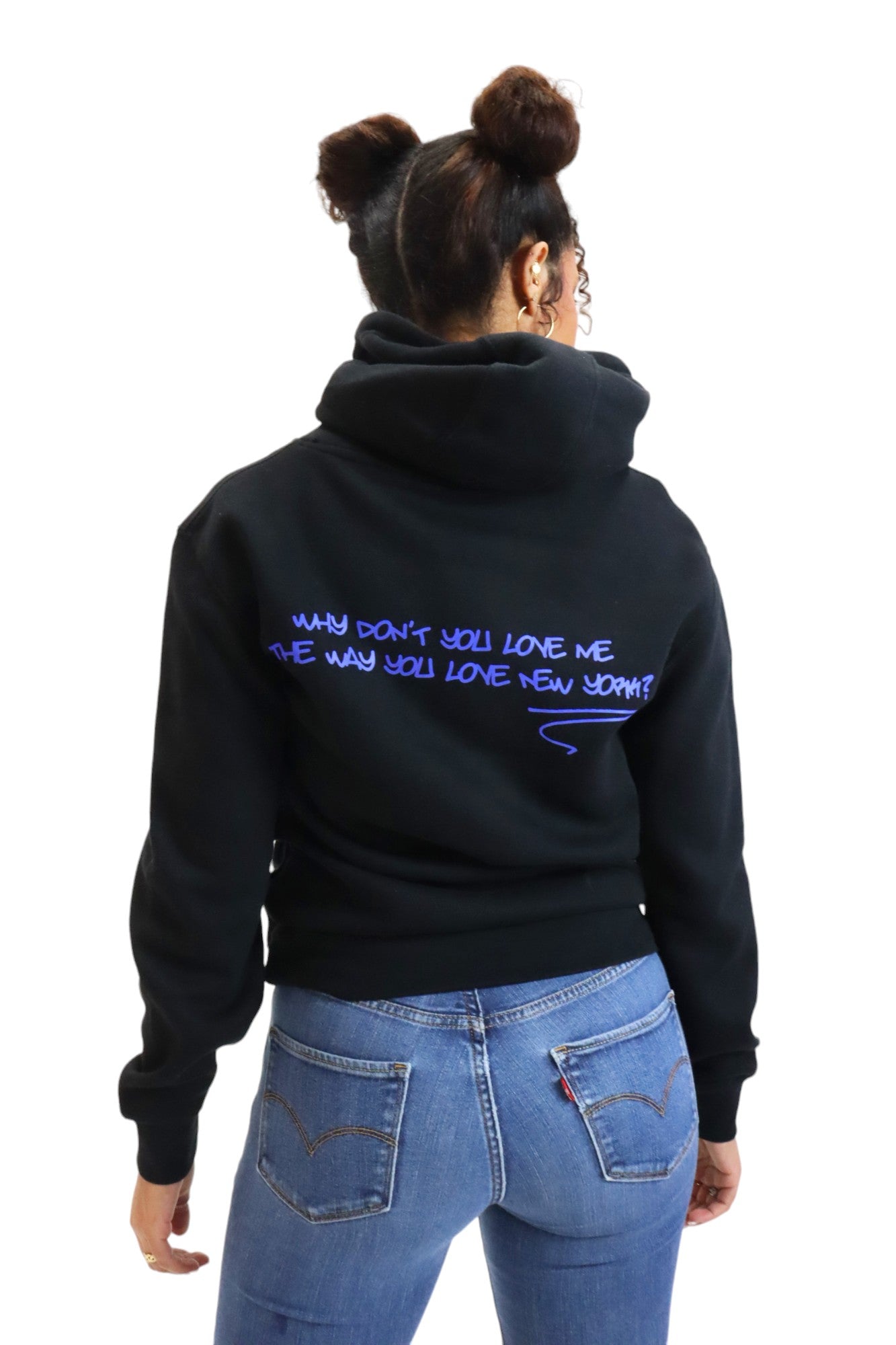 Back view of a woman in a black hoodie. Across the shoulders is the question 'WHY DON'T YOU LOVE ME THE WAY YOU LOVE NEW YORK?' written in a purple graffiti-style font.