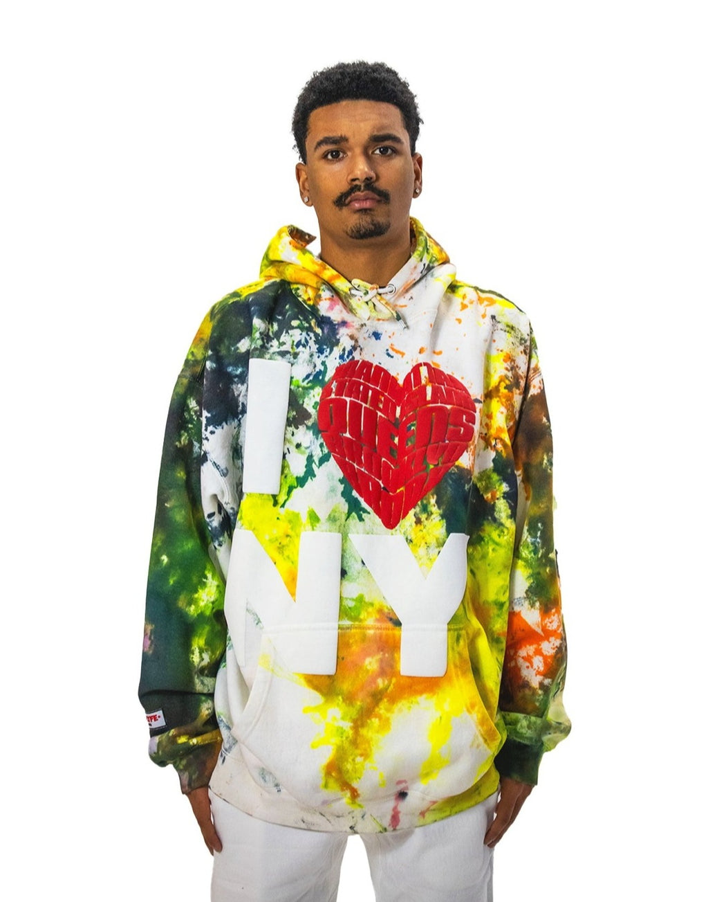 Model wearing a multi-colored ice-dye hoodie with a large, 3D puff-print 'I ❤️ NY' graphic on the front. The red heart has a textured, brick-like pattern.