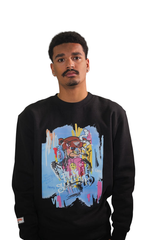 Front view of a model wearing a black crewneck sweatshirt. The sweatshirt features a large, colorful graffiti-style graphic of a cartoon bear with sunglasses against an abstract, chaotic background.