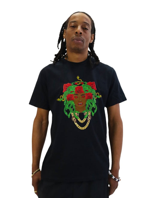 Front view of a model wearing a black t-shirt. The shirt features a large, colorful graphic of Medusa as a Black woman with green snakes and red roses for hair, glowing red eyes, and a gold chain necklace.