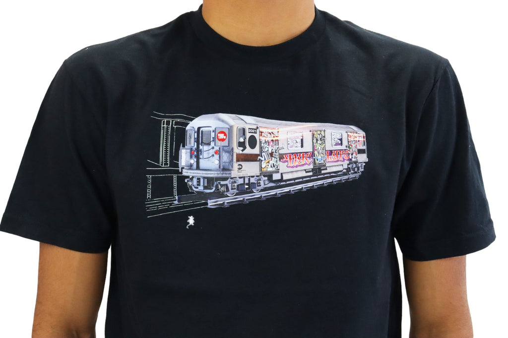 A man models a black t-shirt featuring a detailed graphic of a vintage New York City subway train. The entire side of the train car is covered in colorful, elaborate graffiti as it emerges from a dark tunnel.