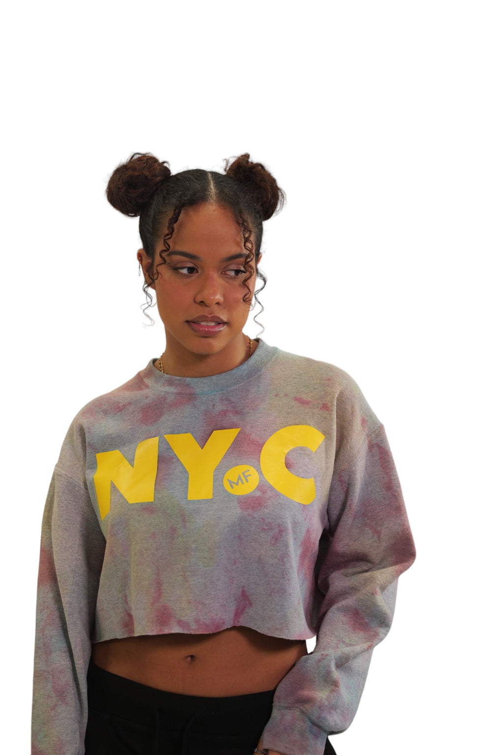 A woman models a long-sleeve cropped crewneck with a grey and pink storm-dye pattern. The letters 'NYC' are printed across the chest in large, bold yellow letters, with a small 'MF' logo inside the letter C.