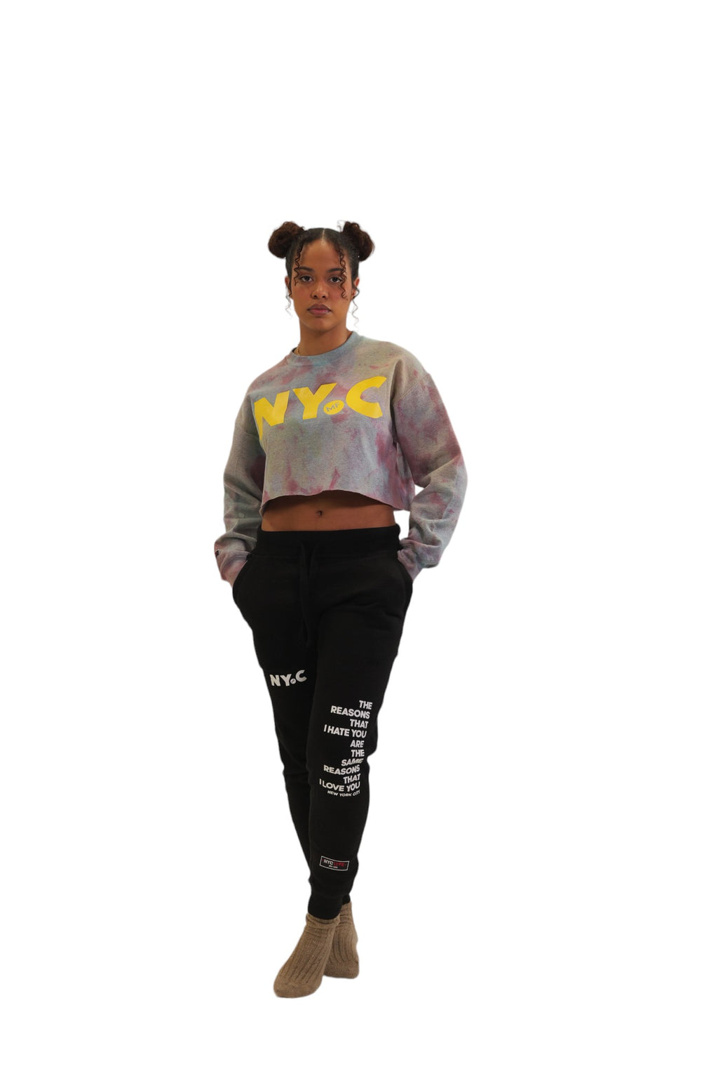 A woman models a long-sleeve cropped crewneck with a grey and pink storm-dye pattern. The letters 'NYC' are printed across the chest in large, bold yellow letters, with a small 'MF' logo inside the letter C.