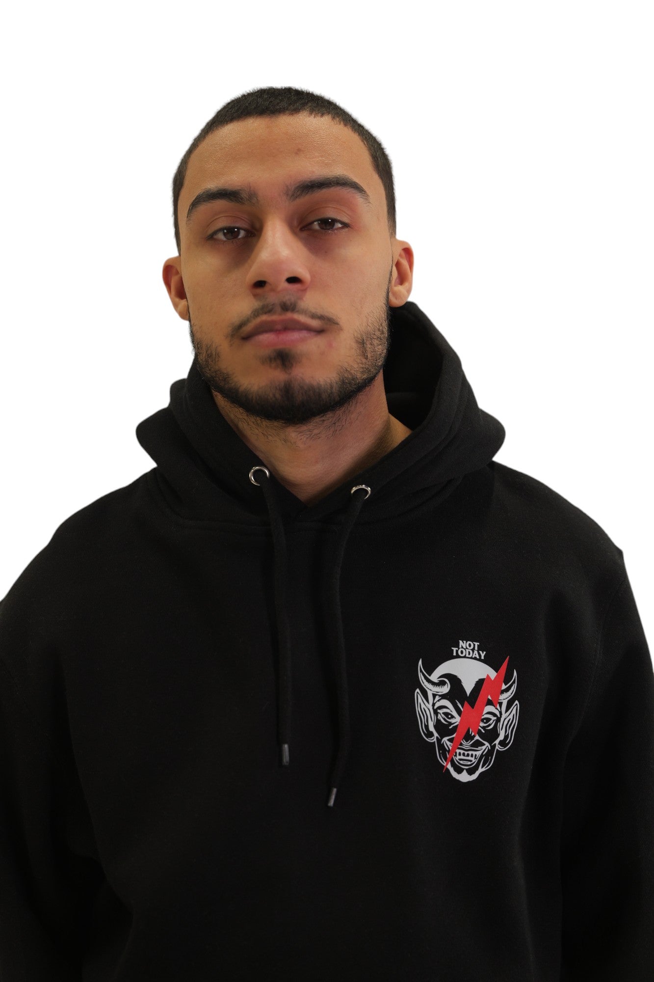 Front close up view of a model wearing a black hoodie with a small graphic on the left chest of a devil's face crossed out with a red X.