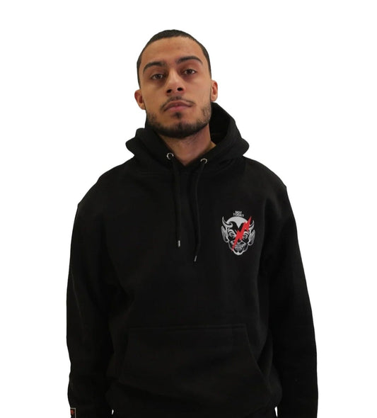 Front view of a model wearing a black hoodie with a small graphic on the left chest of a devil's face crossed out with a red X.